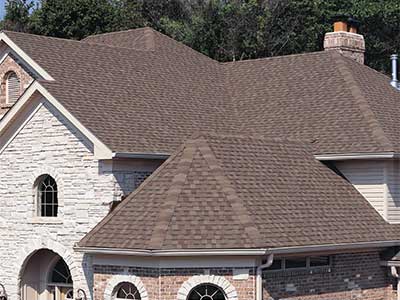 Front view of a large mid-class home brown, red-ish Tamko shingles on its roof