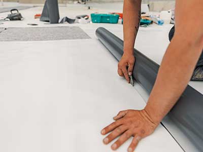 Close up of a worker cutting off a piece of a white TPO sheet