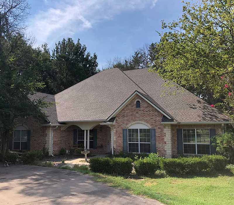 Front view of a mid-class home with new light brown shingles installed by Tejas Roofing & Gutters